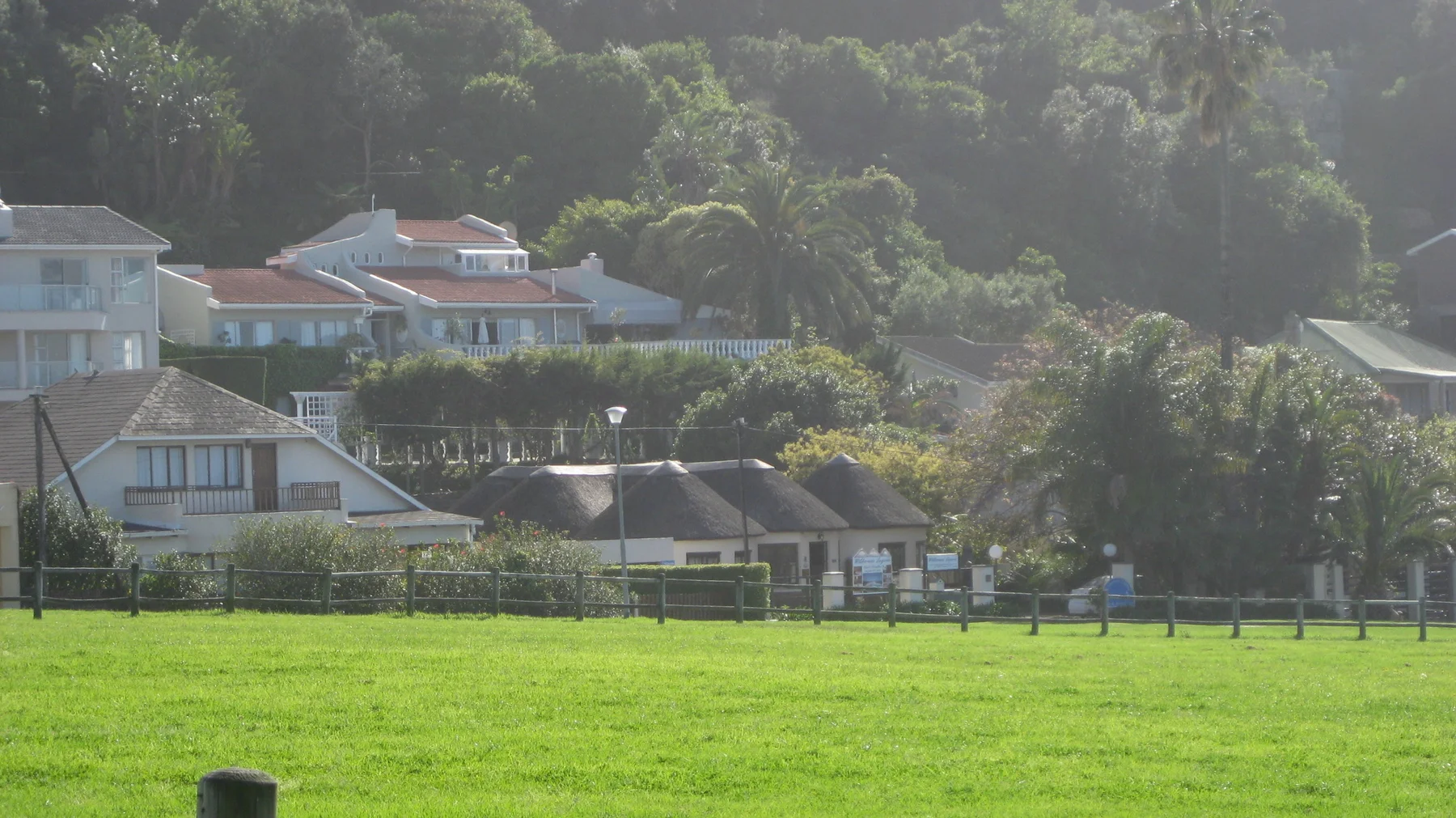 Houses sit below a wooded slope beyond a bright green field.