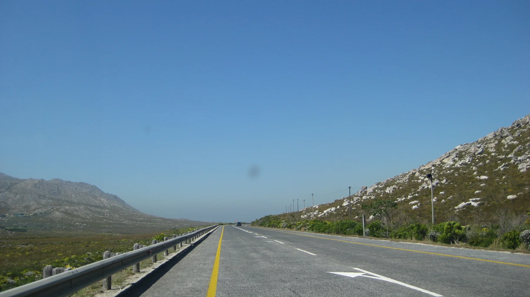 A straight highway runs between rocky green slopes beneath blue sky.