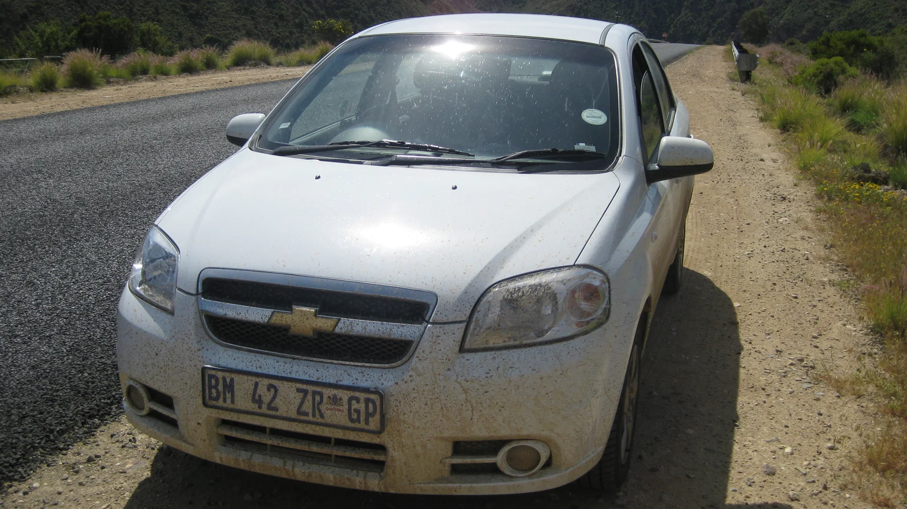 A white car rests on a gravel shoulder beside the road.