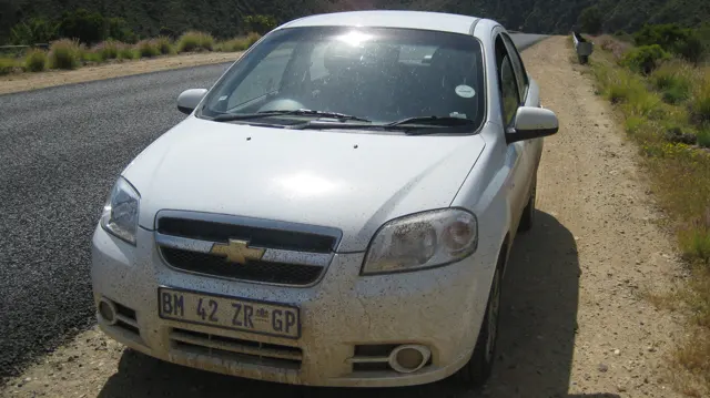 A white car rests on a gravel shoulder beside the road.