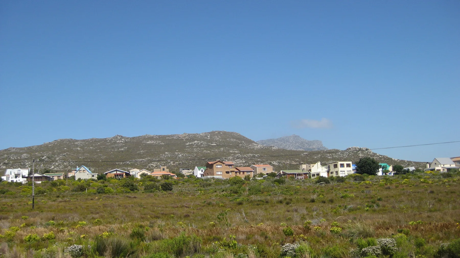 Small houses stand across open scrub below a low mountain ridge.