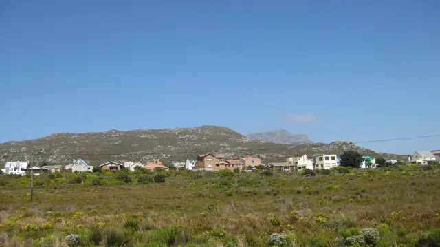 Small houses stand across open scrub below a low mountain ridge.