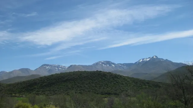 Small snow patches mark distant mountain peaks above green hills.