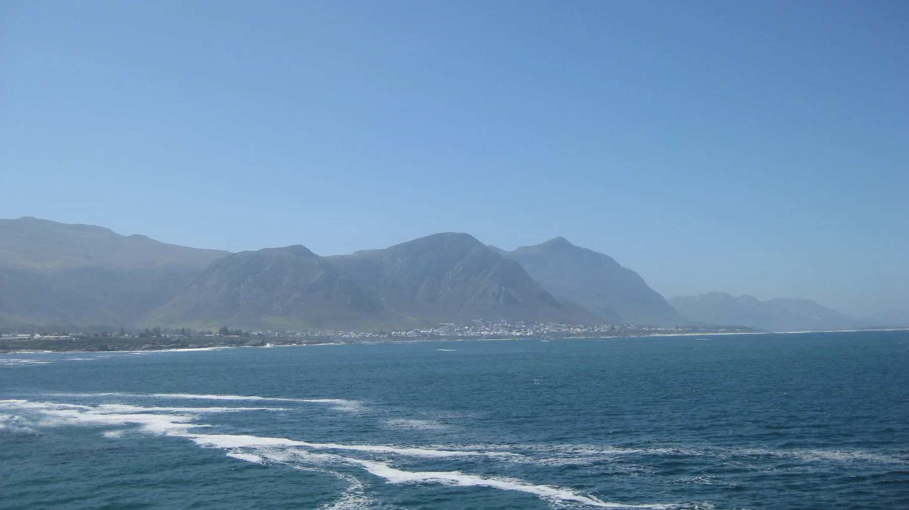 Blue sea and white wave lines stretch below distant mountains.