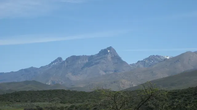 A jagged rocky peak rises beyond rounded green hills.