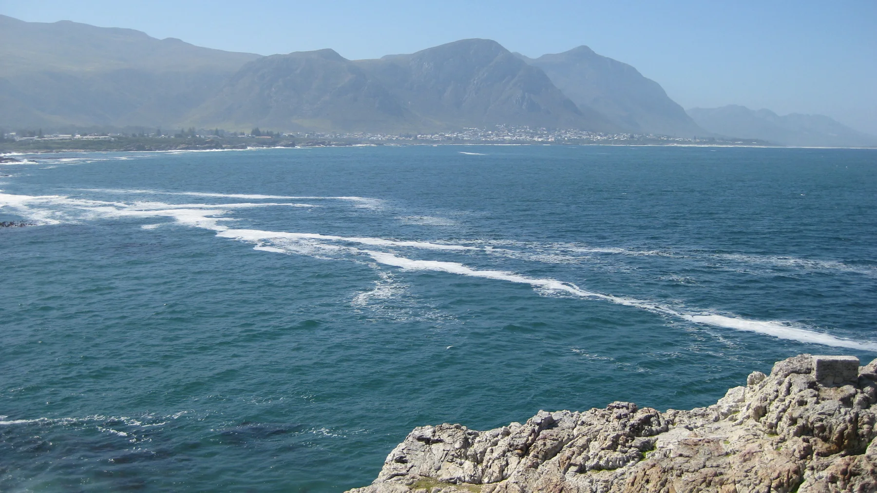 White waves cross blue water beyond a pale rocky ledge.