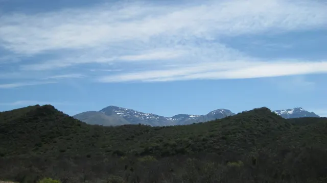 Distant high peaks rise behind dark green ridges and thin clouds.