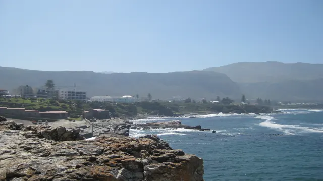 Coastal buildings stand behind rocky shoreline and blue water.