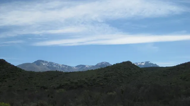 Snow-dotted peaks rise beyond dark low hills beneath streaked clouds.