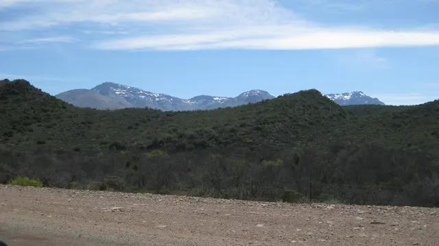 A gravel verge borders layered green hills and distant pale peaks.