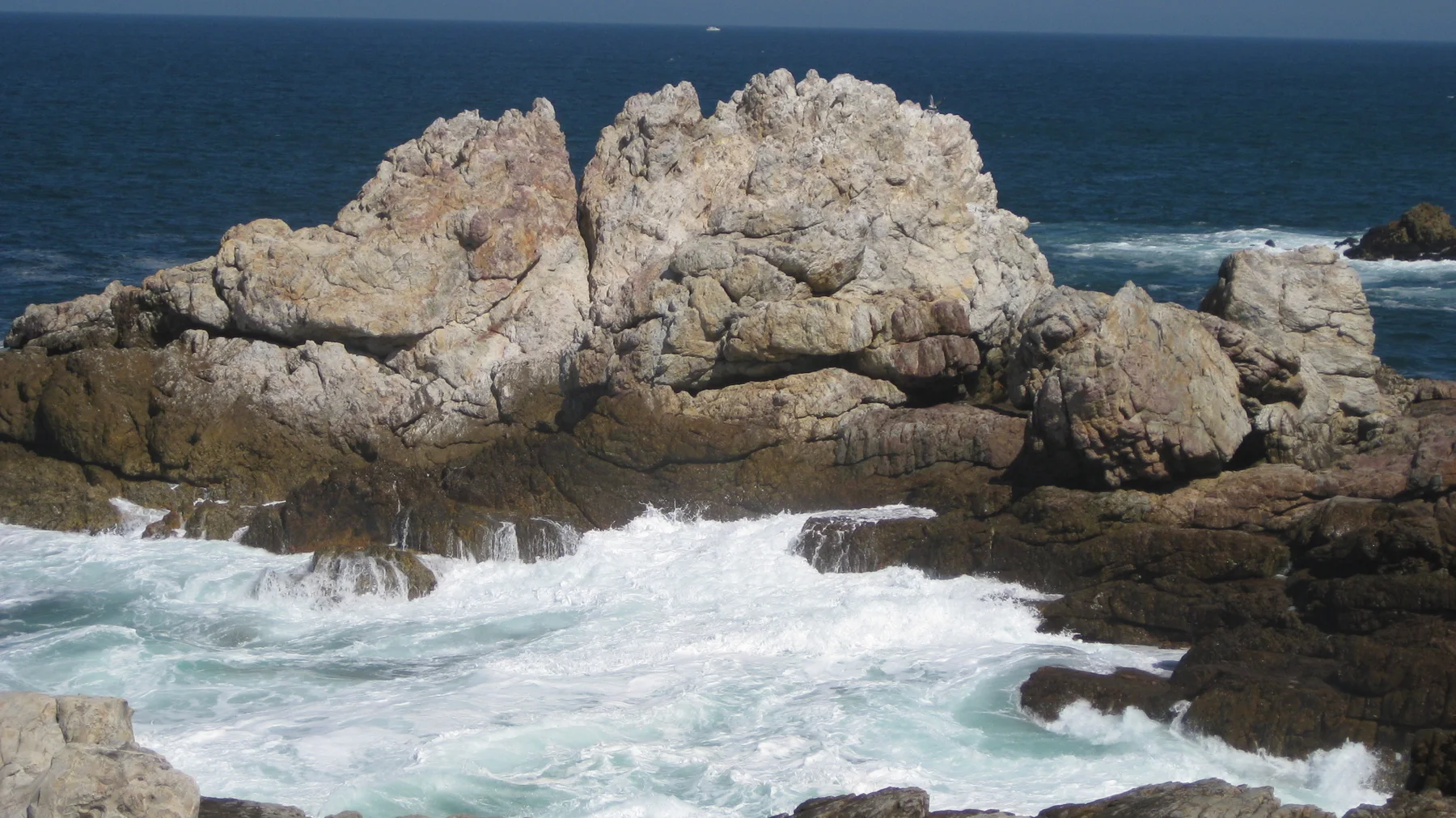 White water surges beneath pale angular coastal rocks.