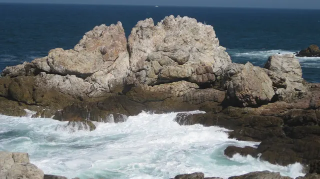White water surges beneath pale angular coastal rocks.