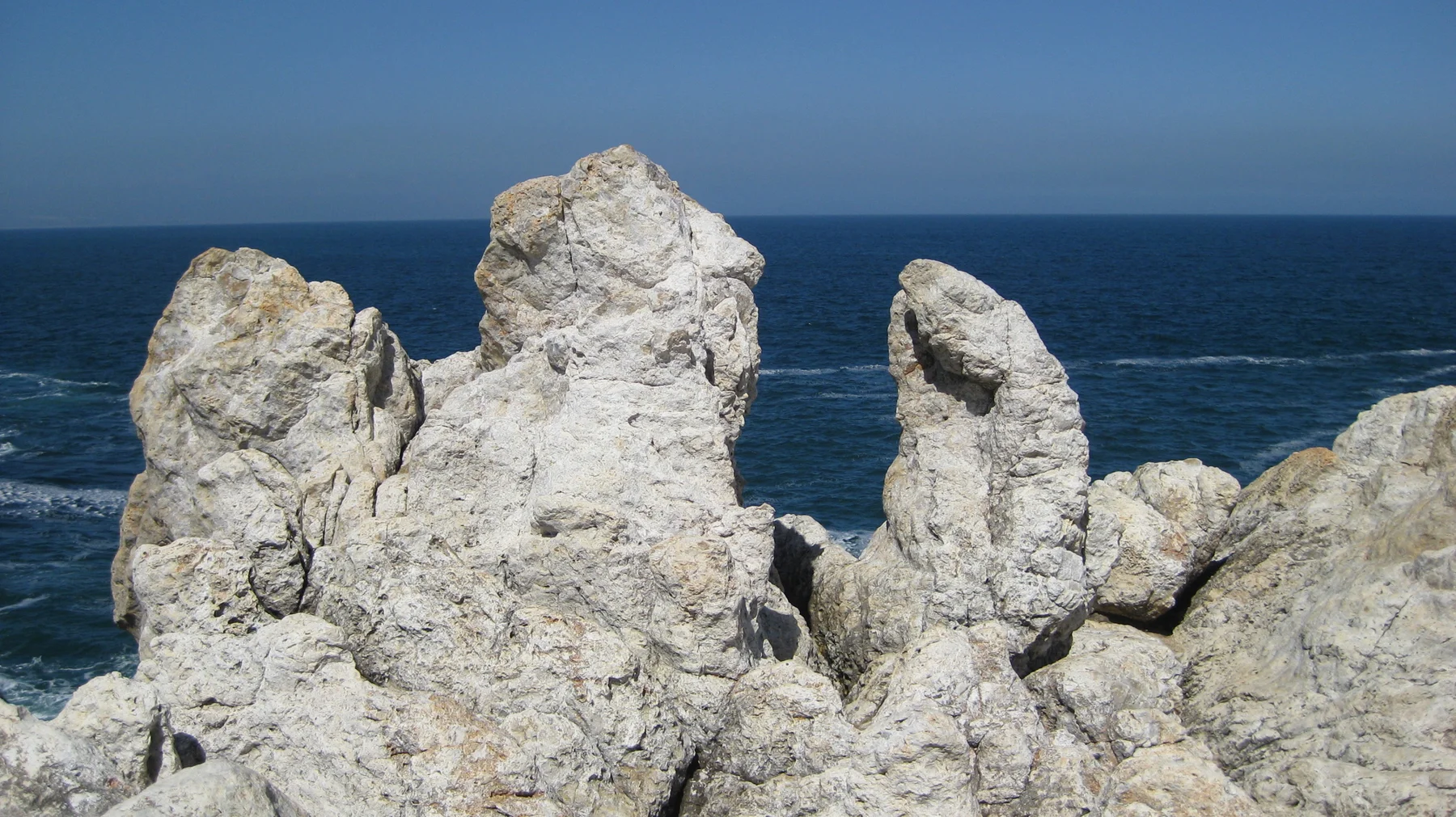 Pale jagged rocks rise against deep blue ocean.