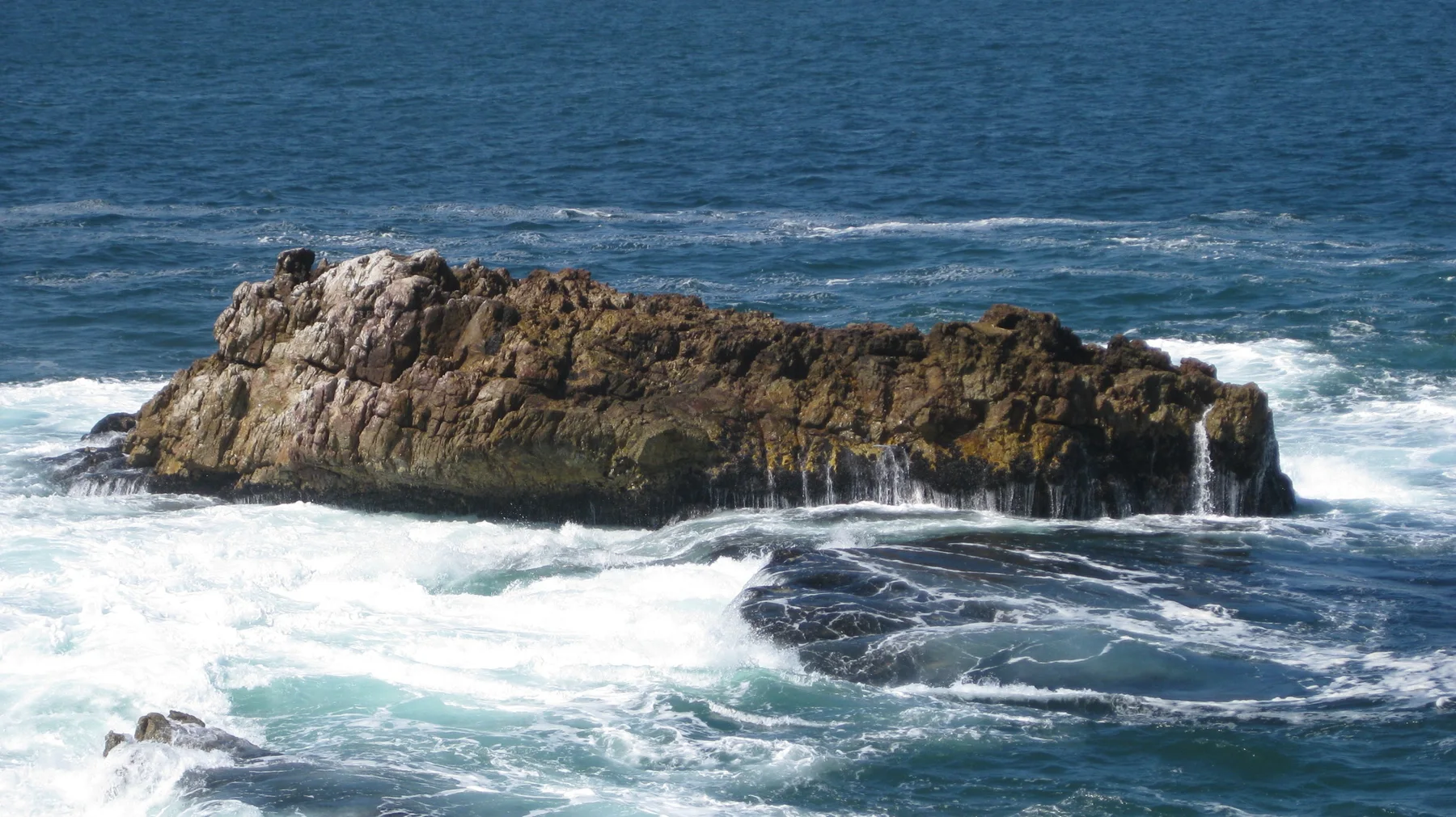 White water drains from a low brown offshore rock.