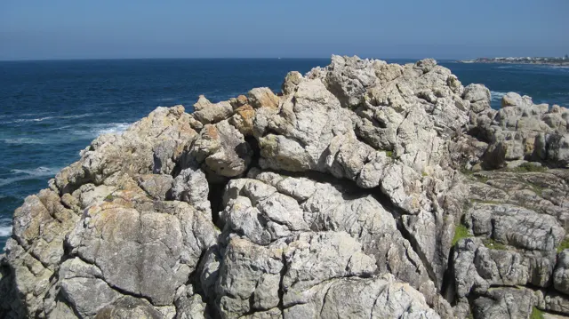 A broken pale rock formation stands above blue water.