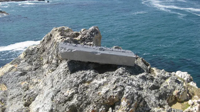A simple bench rests on pale rocks above blue water.