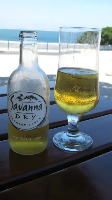 A bottle and glass of golden drink stand beside a sea-facing window.