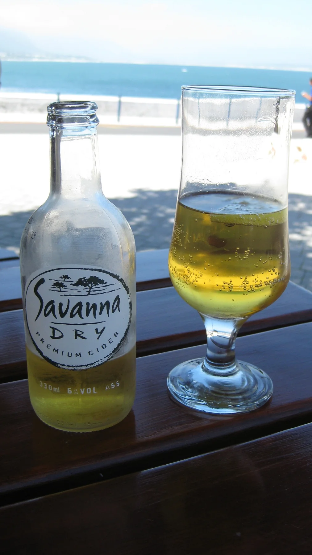 A filled glass and labeled bottle sit before a bright coastal view.