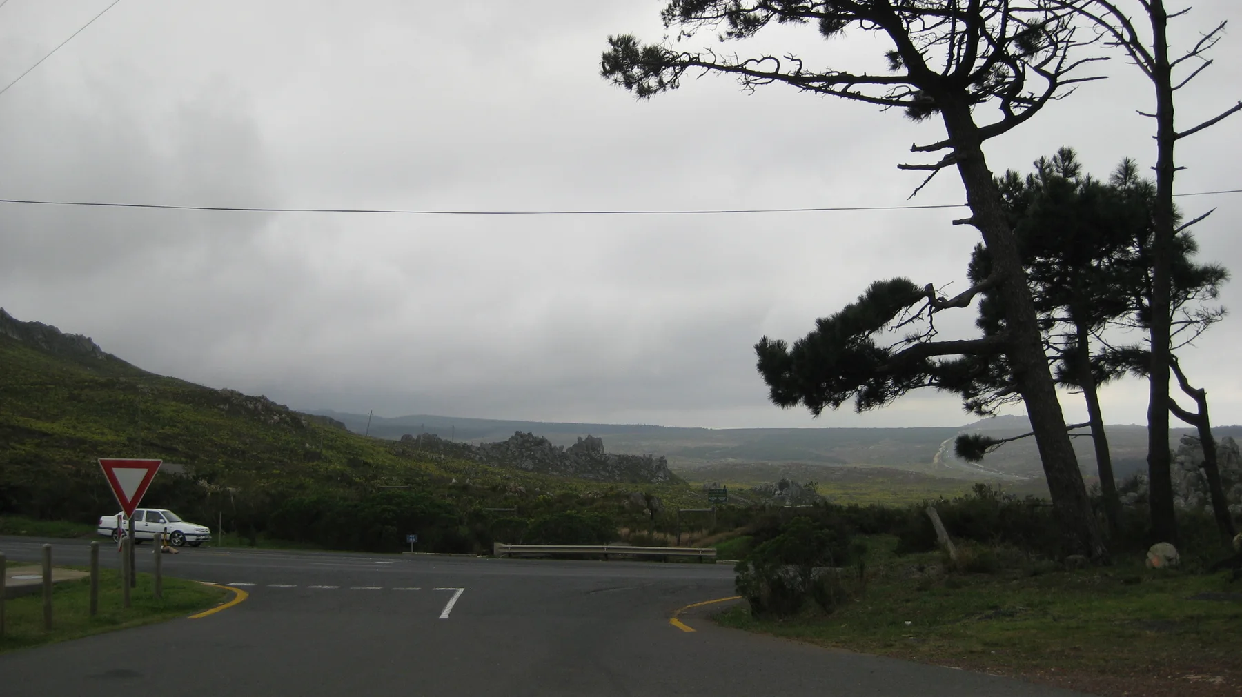 A road meets a junction beside dark trees and clouded hills.