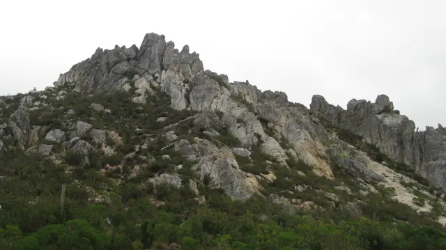 Jagged rocks crown a green knoll beneath gray sky.