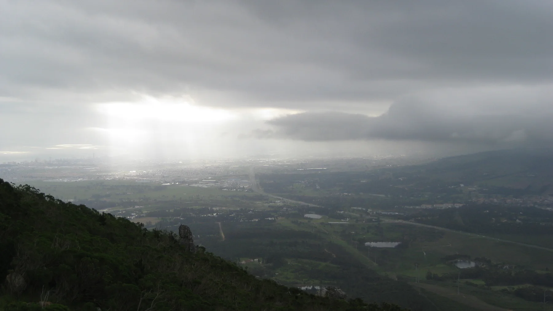Sunbeams break through dark clouds above a distant valley.