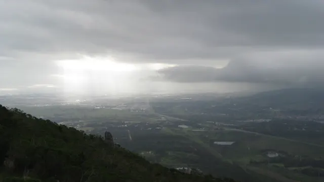 Sunbeams break through dark clouds above a distant valley.
