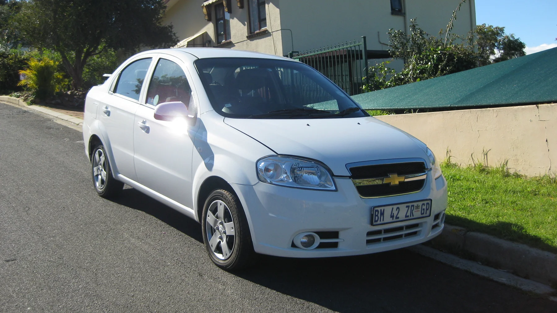 A white car is parked beside a pale garden wall.