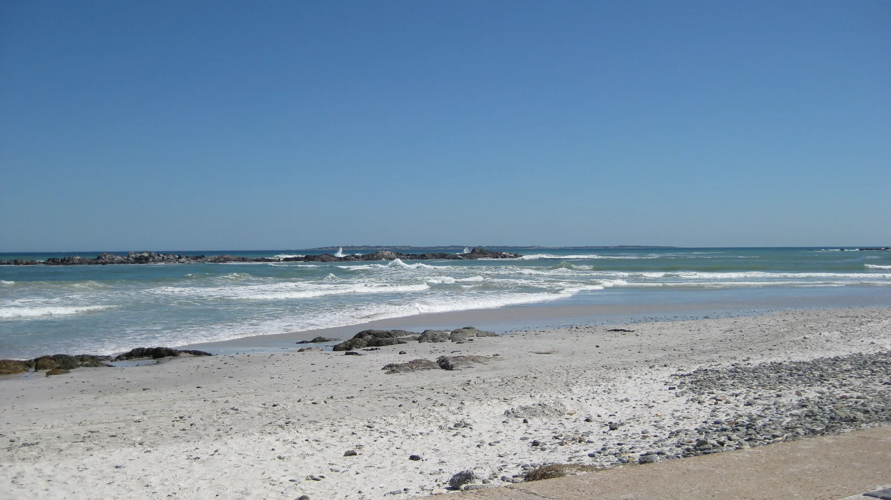 Low waves cross a shallow beach scattered with dark rocks.