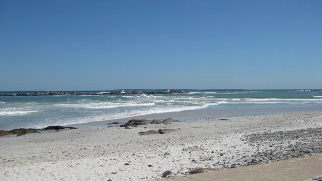 Low waves cross a shallow beach scattered with dark rocks.