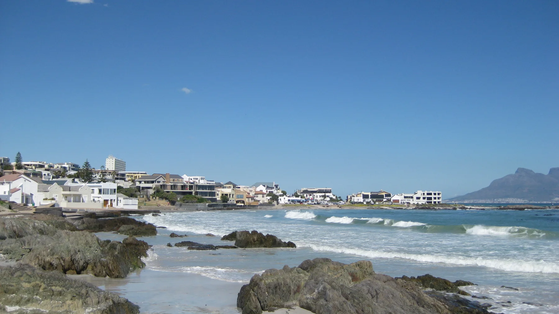 Pale coastal buildings stand above rocks and rolling surf.
