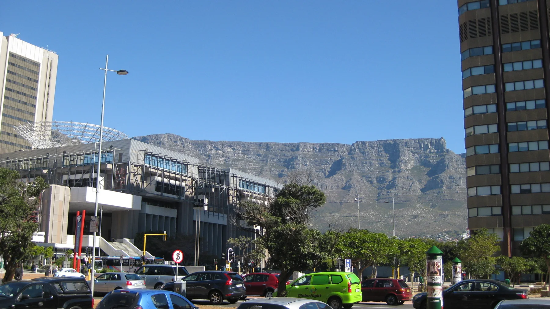 City traffic passes a modern building below a flat mountain ridge.
