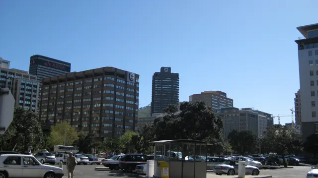 Office towers rise above a parking area and leafy trees.