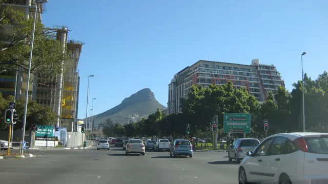 Traffic crosses a broad intersection with a pointed hill beyond.