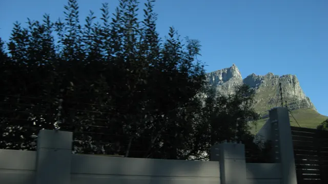 A rocky peak appears above dark trees and a garden wall.