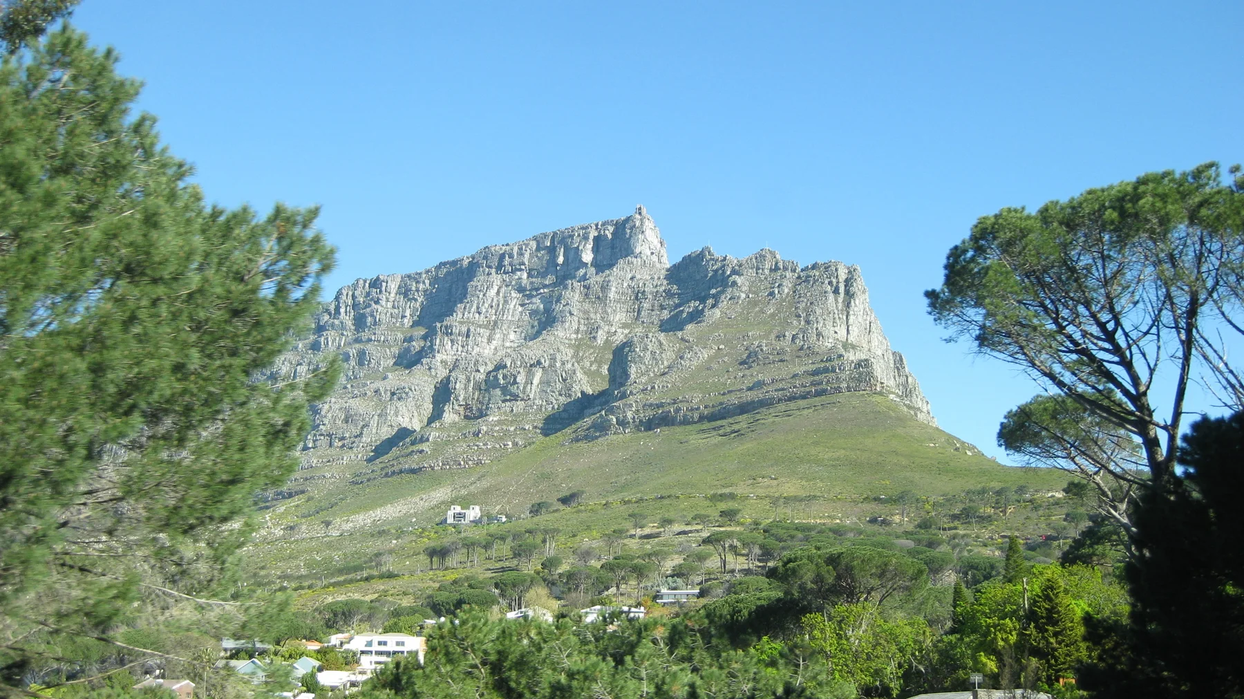 Sunlit cliffs rise above green slopes between foreground trees.