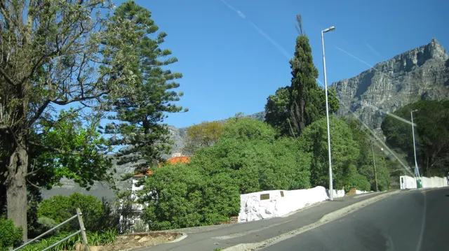 A narrow street climbs beside a white wall and dense greenery.