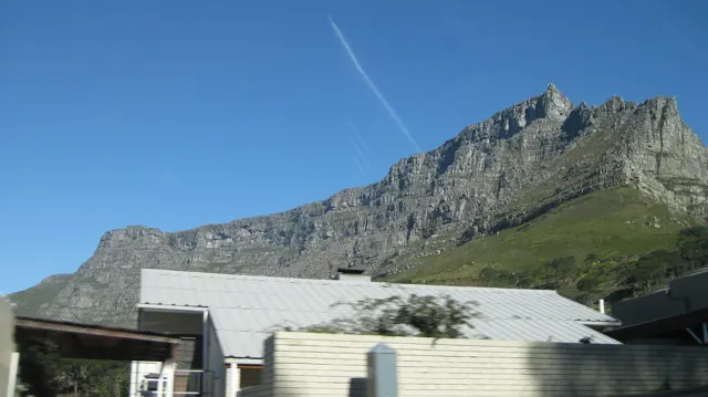 Low roofs sit beneath a long steep mountain wall.
