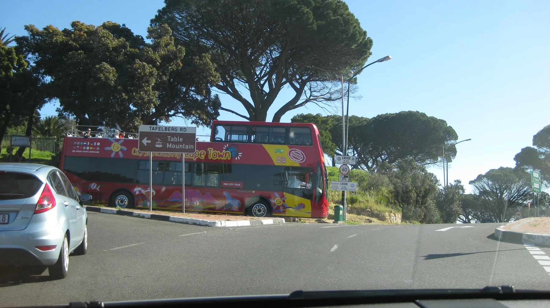 A red double-decker sightseeing bus stands beside a tree-lined road.