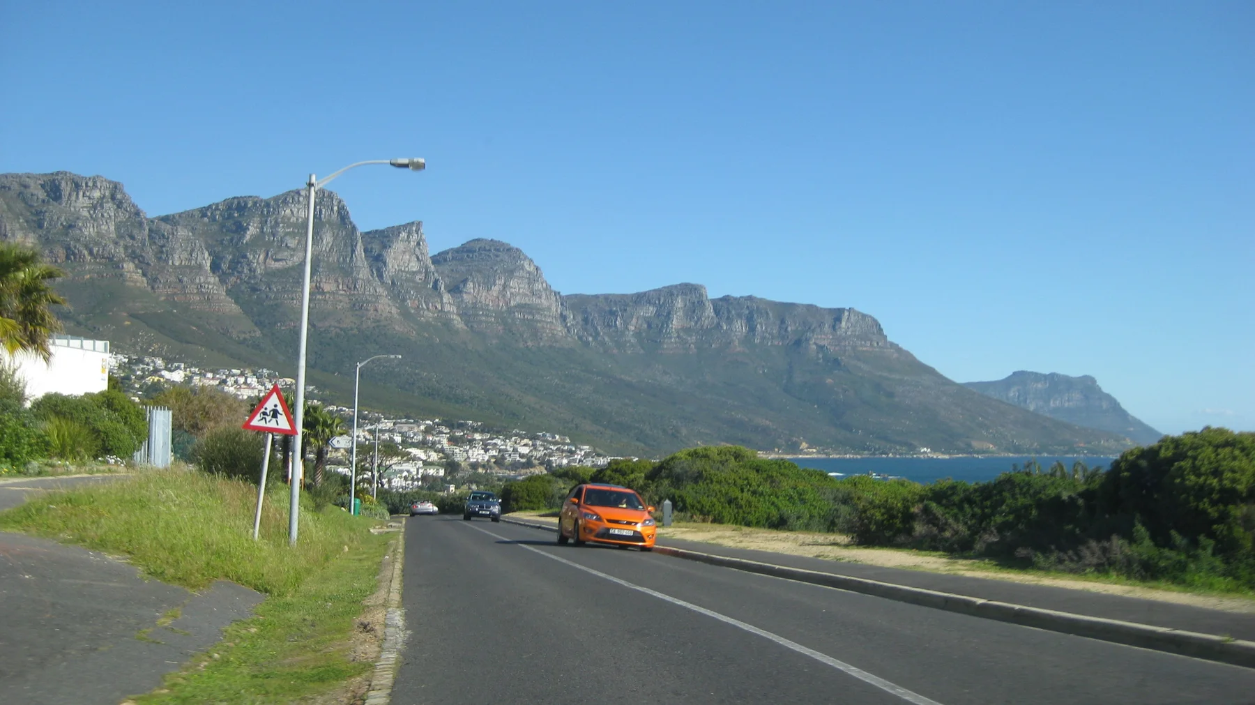 An orange car travels below a long jagged mountain ridge.