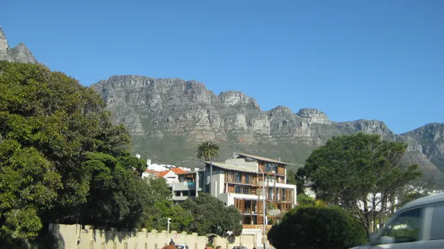 Buildings nestle among trees beneath steep gray cliffs.