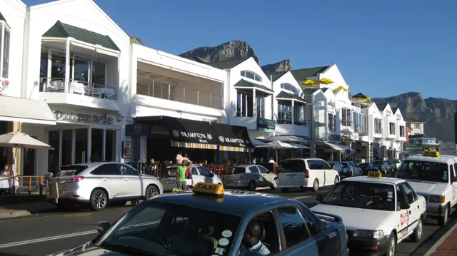Cars line a street beside white shops with peaked roofs.