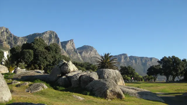 Rounded boulders rest on grass below steep mountains.