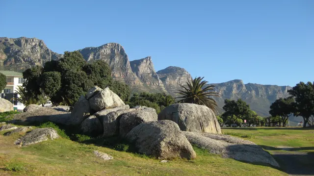 Pale boulders interrupt a green lawn with mountains behind.