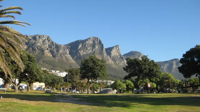 A green park lies below jagged mountain crags.