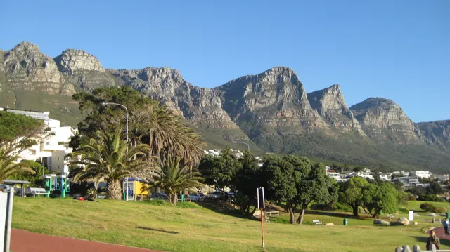 A broad green lawn stretches toward palms and rugged mountains.