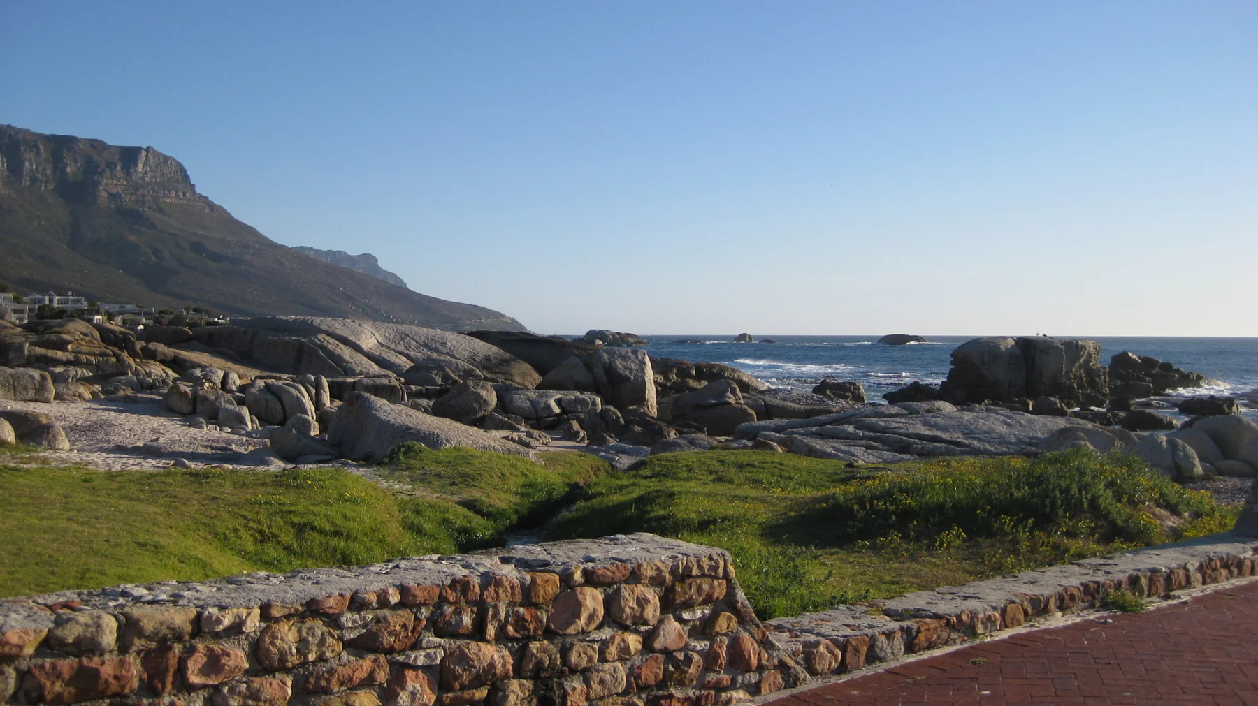 Green grass and dark rocks border a rugged coastal strip.
