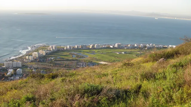 An oval stadium and nearby buildings lie below a green hillside.