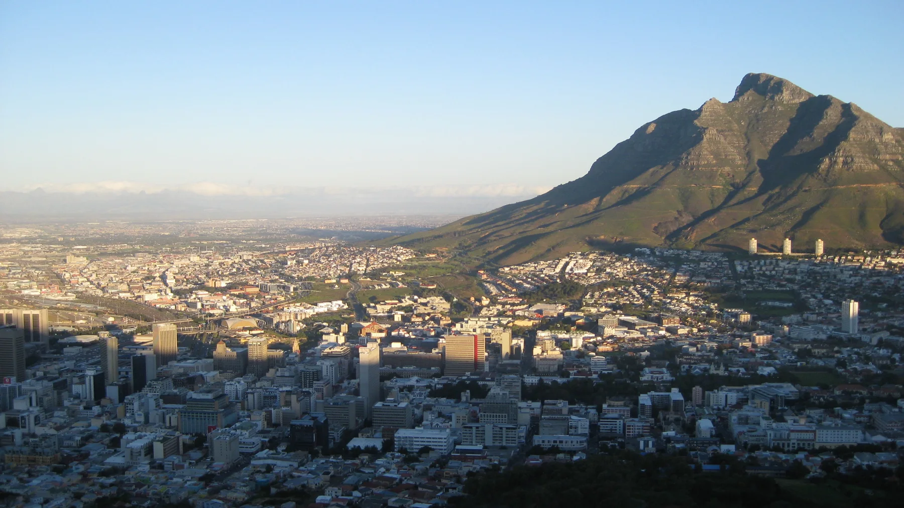 Warm light falls across city blocks below a steep mountain.