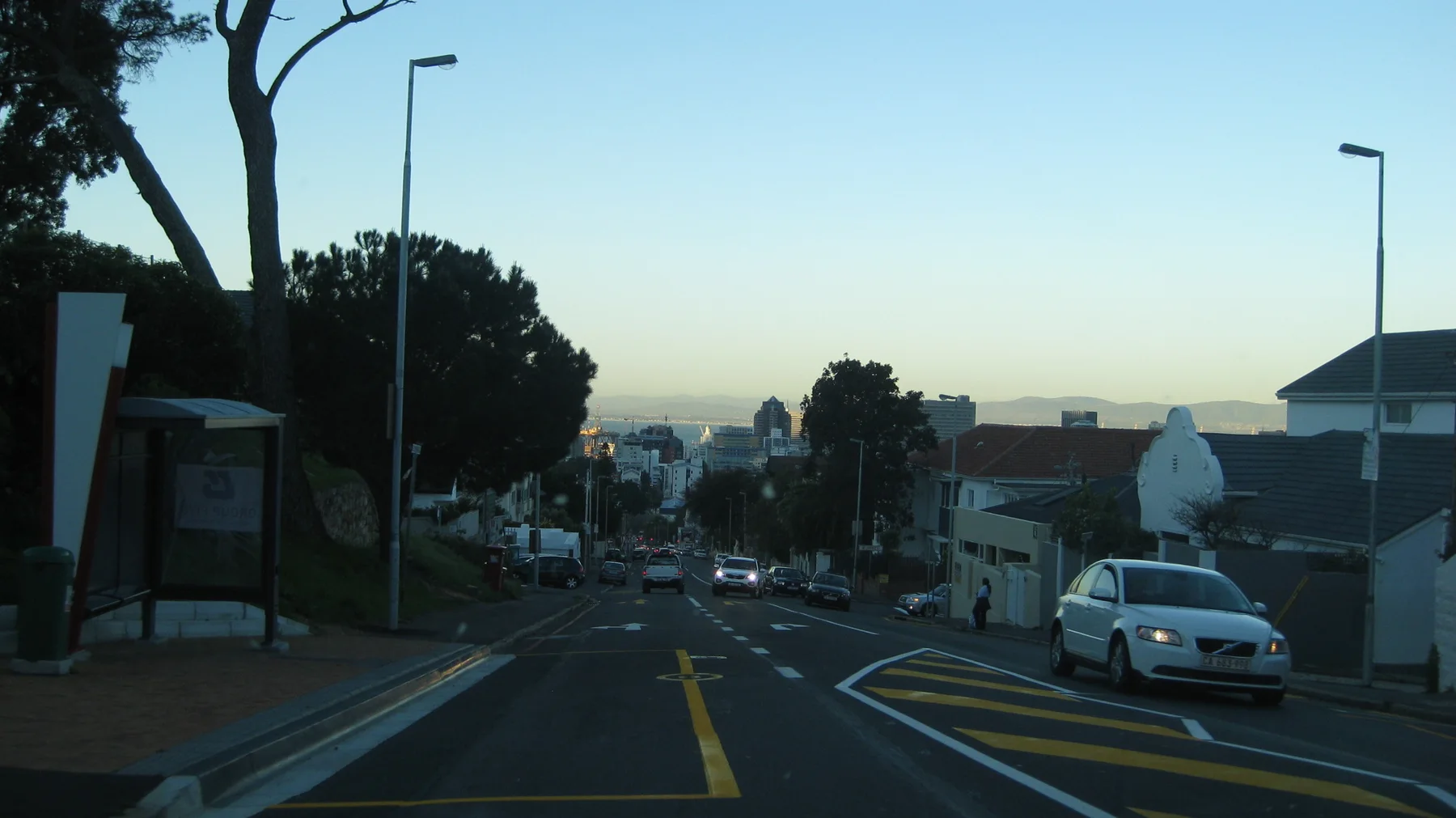 A residential street slopes past parked cars in fading light.