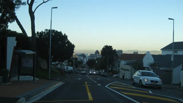 A residential street slopes past parked cars in fading light.